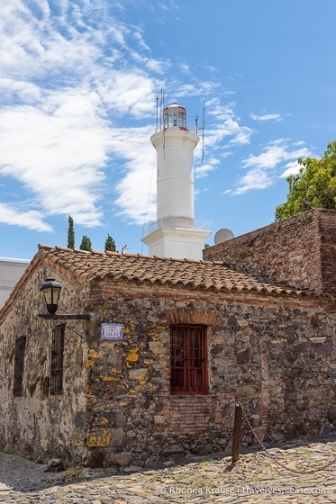 Casa de piedra con el faro de Colonia del Sacramento al fondo.